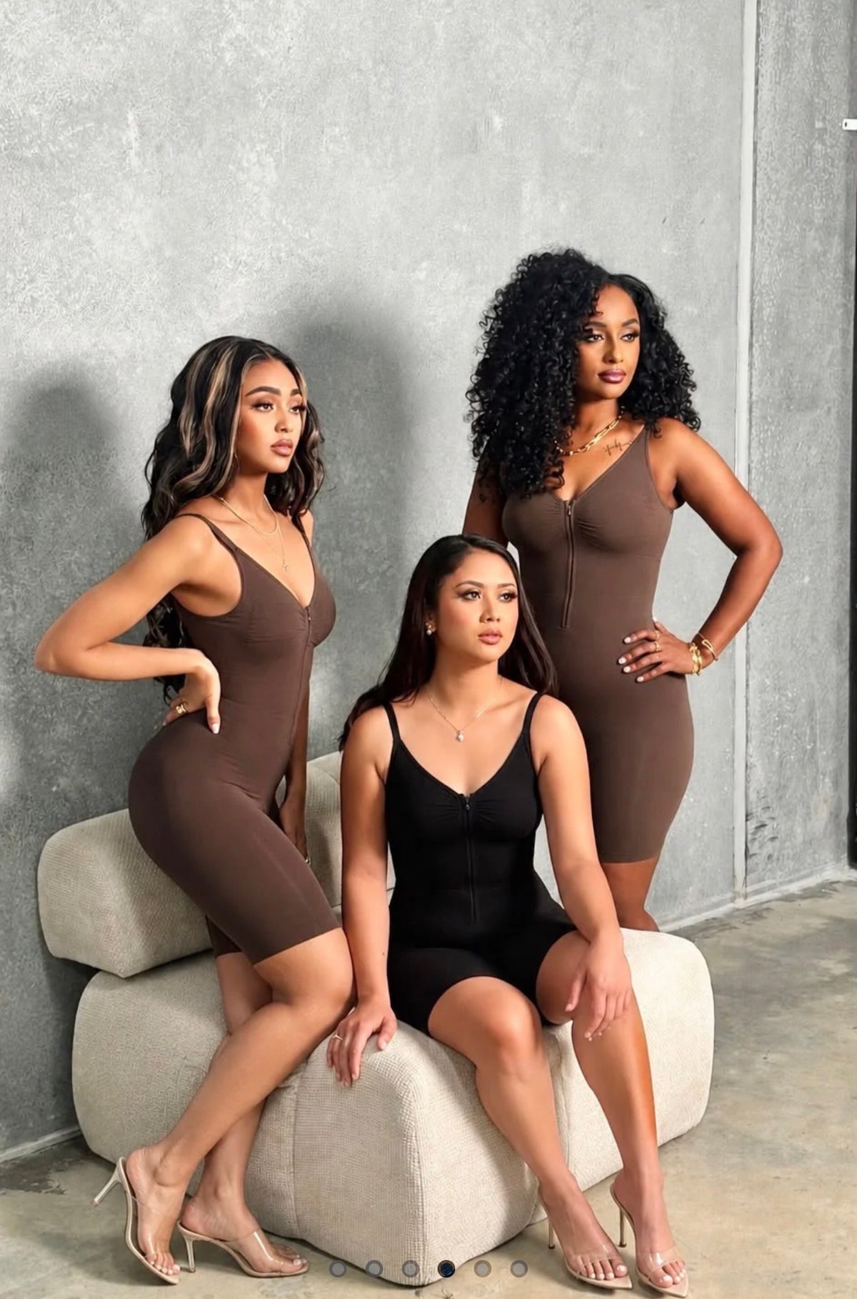 Three women wearing brown and black zip mid thigh bodysuits.